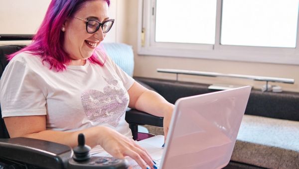 Woman entrepreneur in wheelchair smiling and interacting with business network on laptop